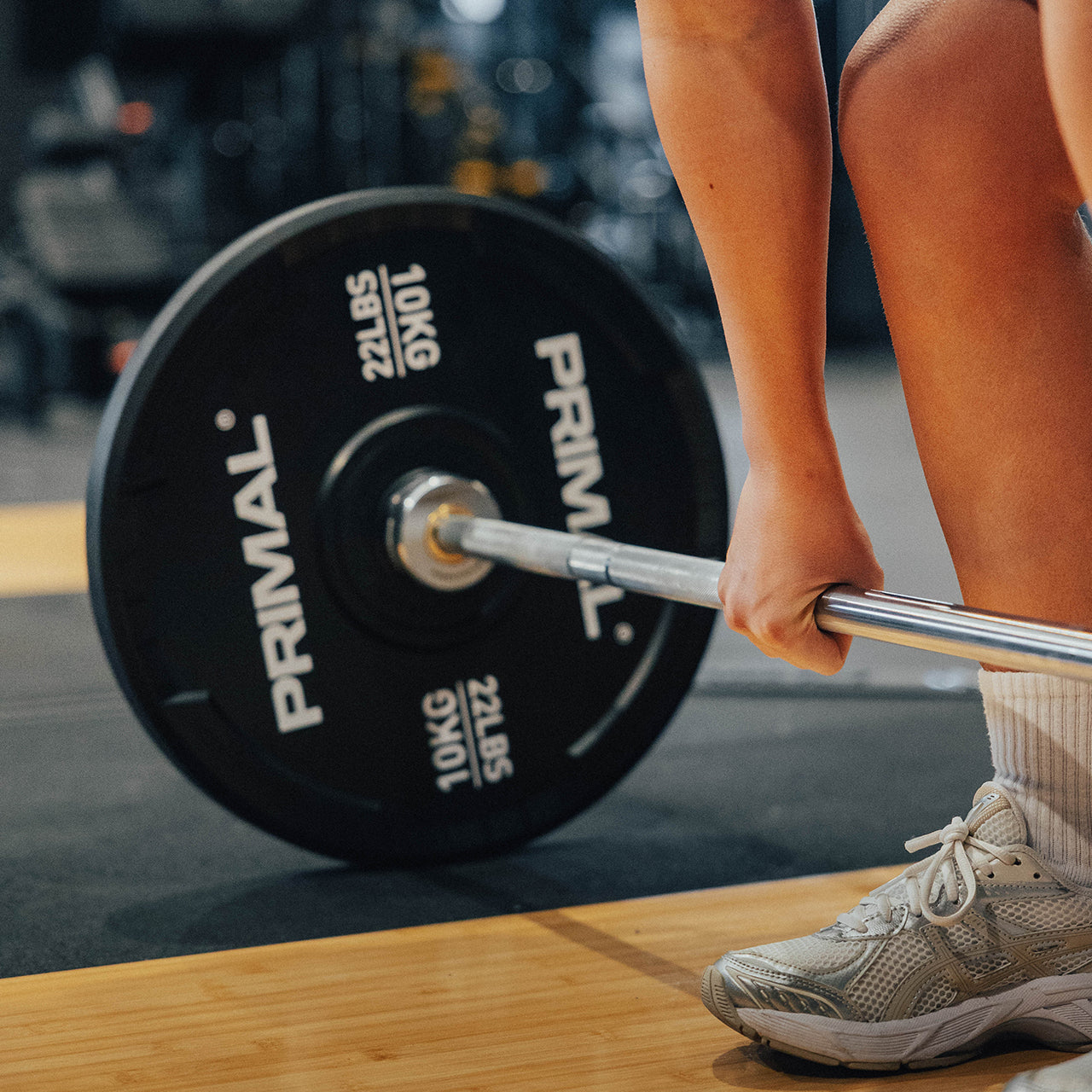 Person lifting a barbell with Primal weight plates in a gym setting