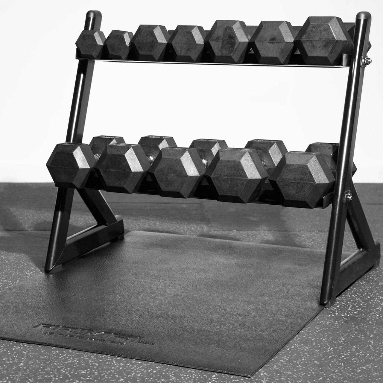A 2-tier rack filled with hex dumbbells on a mat in a gym.