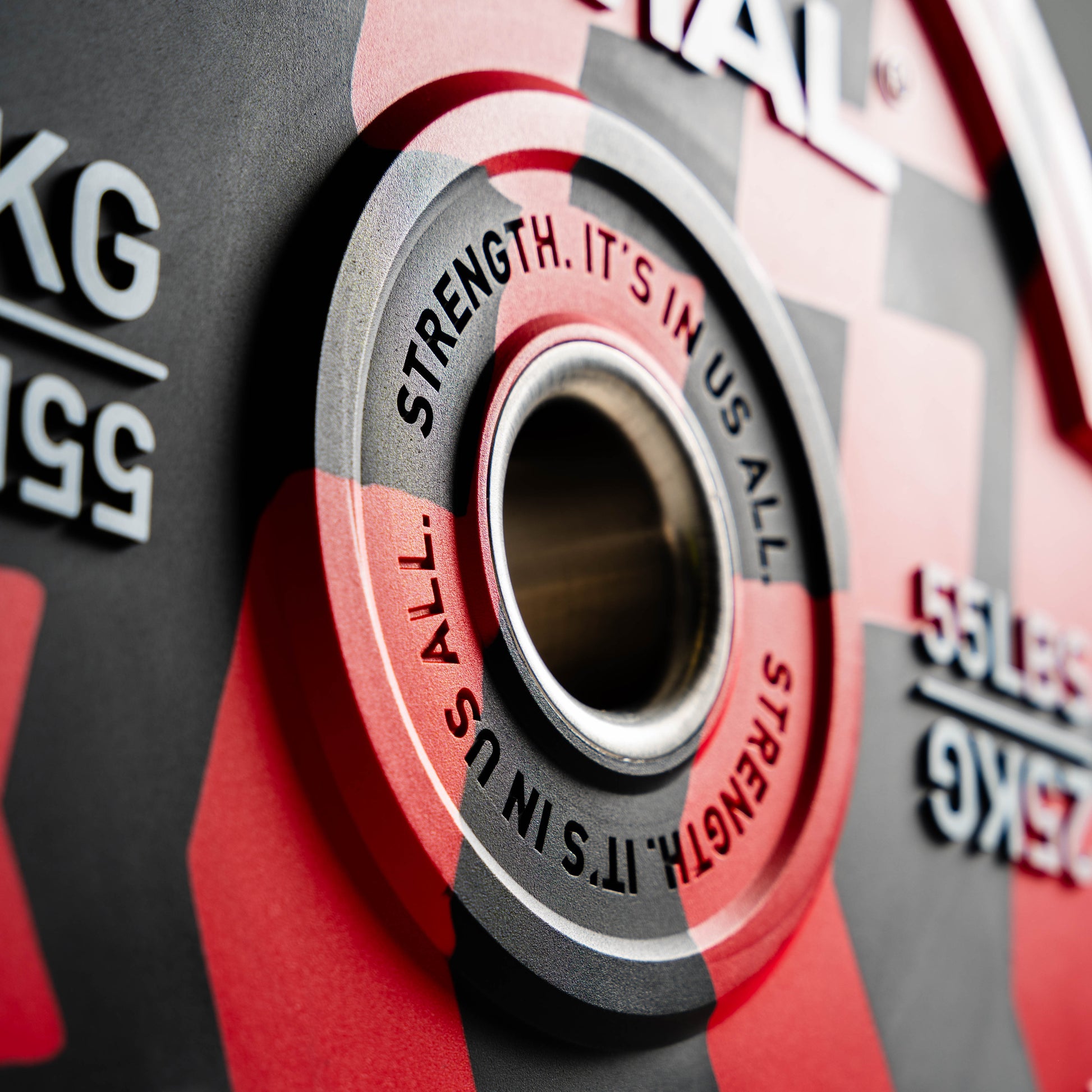 Close-up of a red and gray weight plate with 'Strength. It's in us all' text.