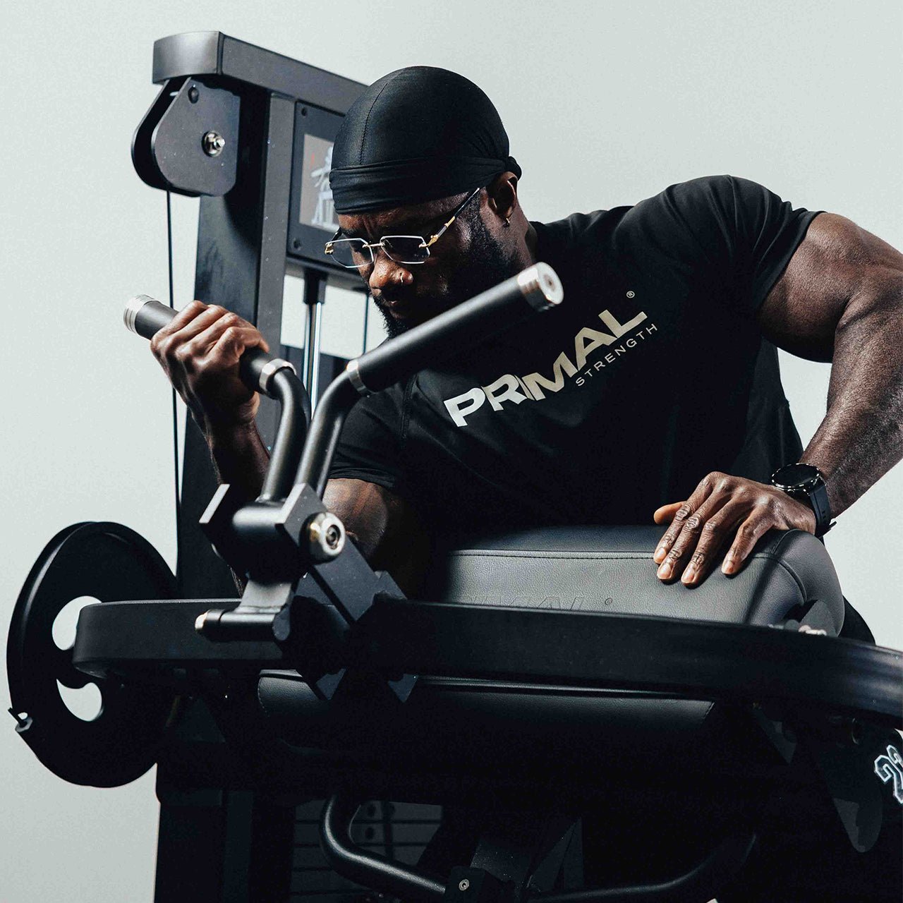 Man wearing a 'Primal Strength' shirt using a bicep curl machine.