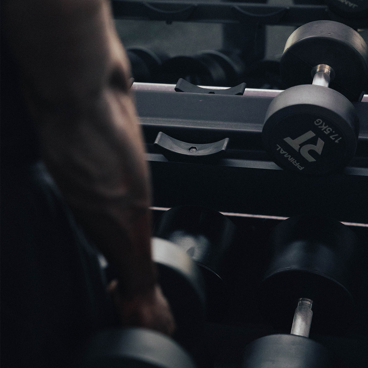 An athlete lifting a round dumbbell off a dumbbell rack.