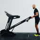 Man setting up a Primal folding treadmill against a white wall.