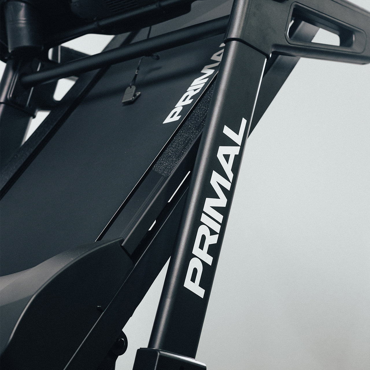 Close-up of a folding treadmill frame with 'Primal' branding on a light gray background