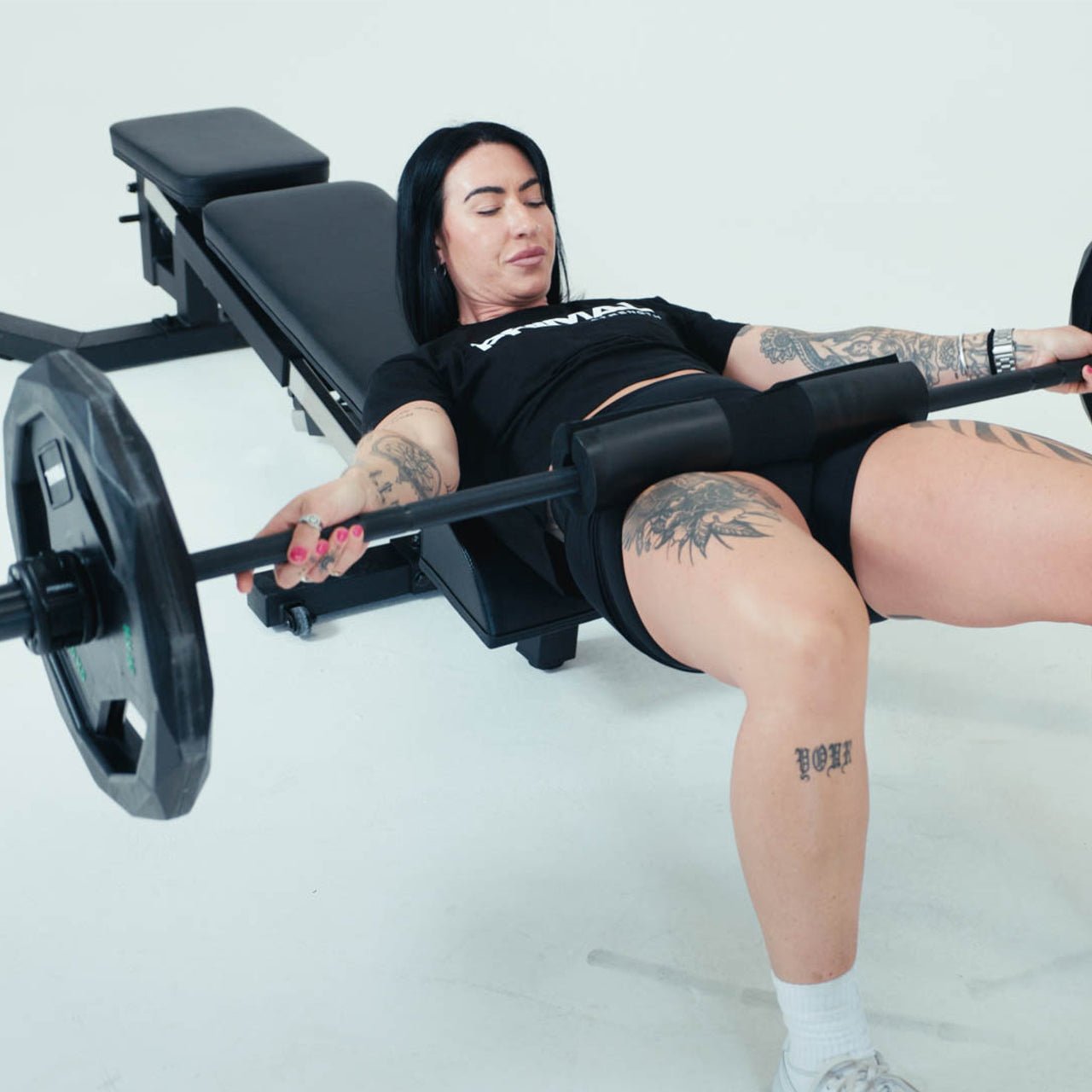 An athlete using a hip thrust pad attachment with barbell on a weight bench.