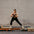 Woman in black athletic wear performing a yoga pose on a reformer against a brick wall.