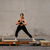 Woman in black athletic wear performing a yoga pose on a reformer against a brick wall.
