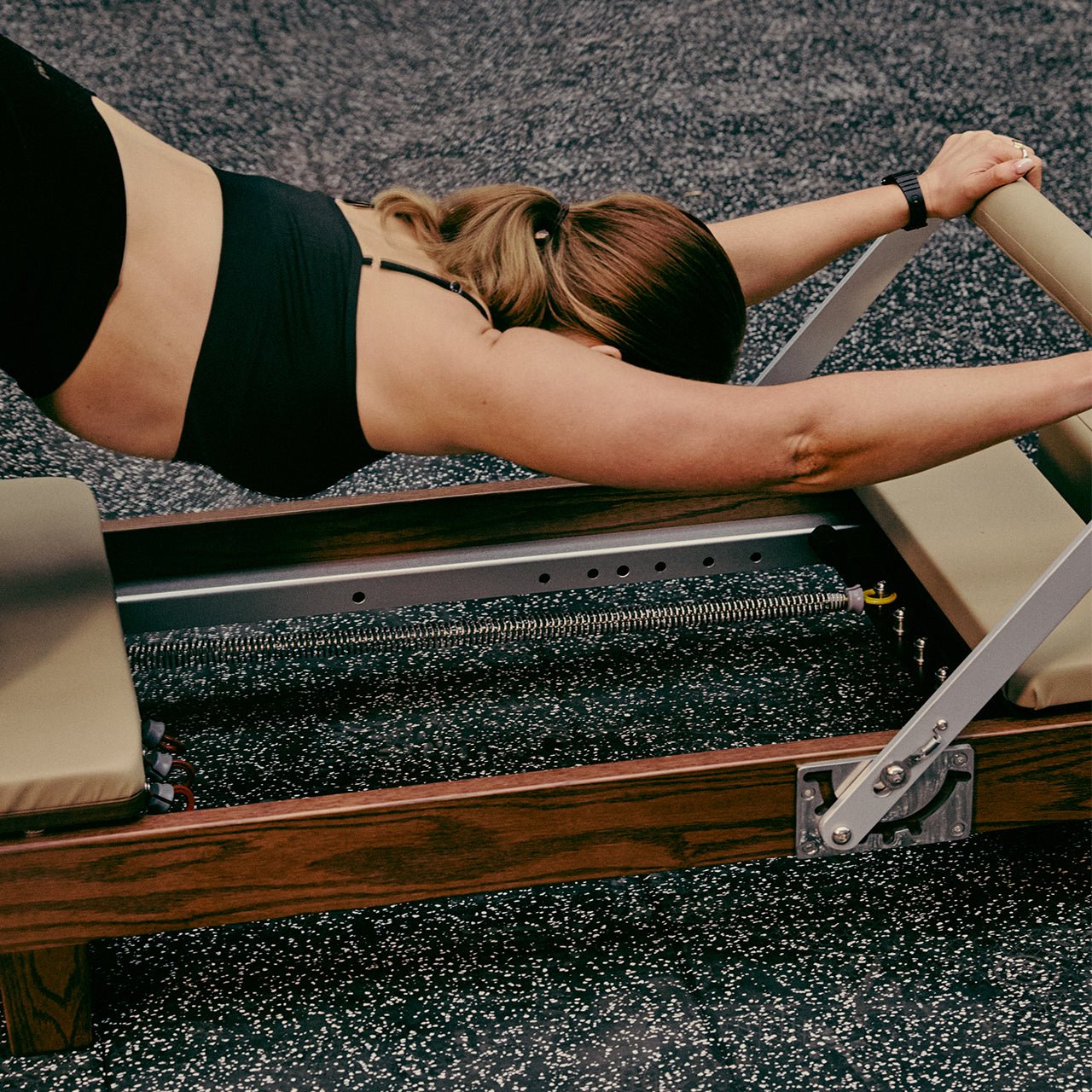Person using a Pilates reformer machine in a gym setting.