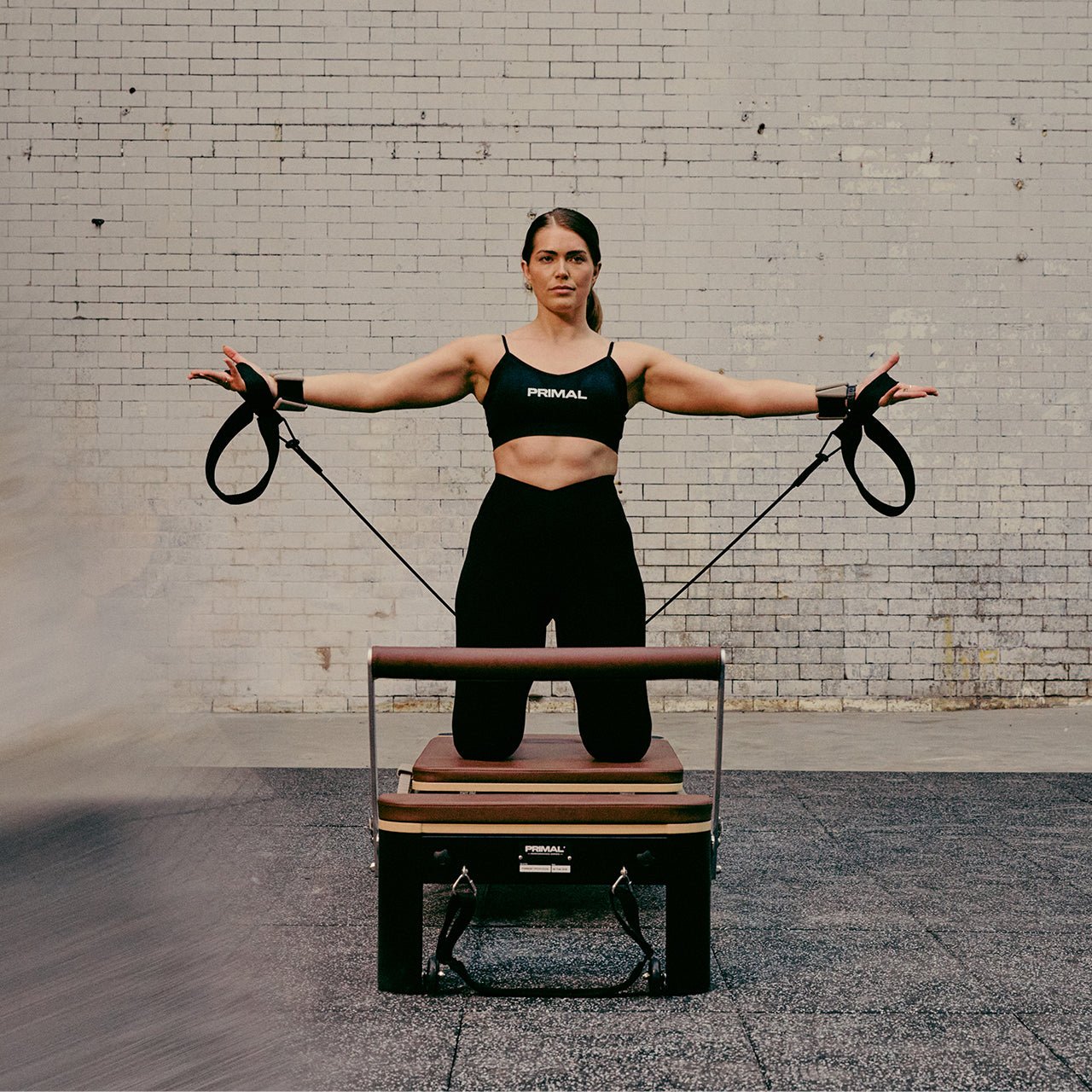 Woman exercising with Pilates reformer against a brick wall.