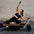 Woman exercising on a Pilates reformer machine against a brick wall.