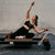 Woman exercising on a Pilates reformer machine against a brick wall.