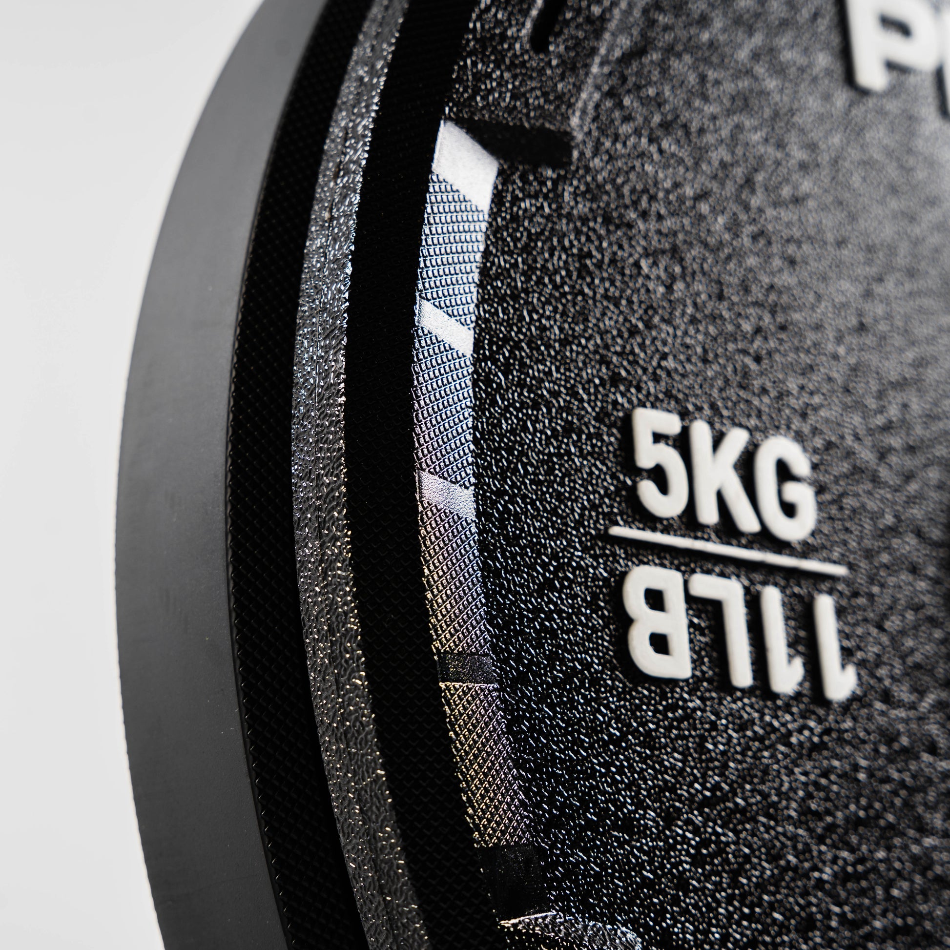 Close-up of a black weight plate with '5KG' and '11LB' text on a gray background
