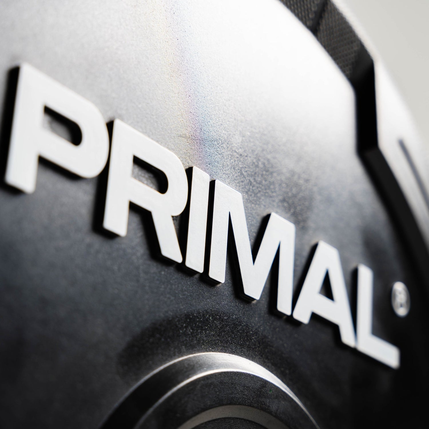 Close-up of a 'PRIMAL' logo on a black rubber bumper plate