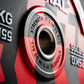 Close-up of a red and gray weight plate with 'Strength. It's in us all' text.