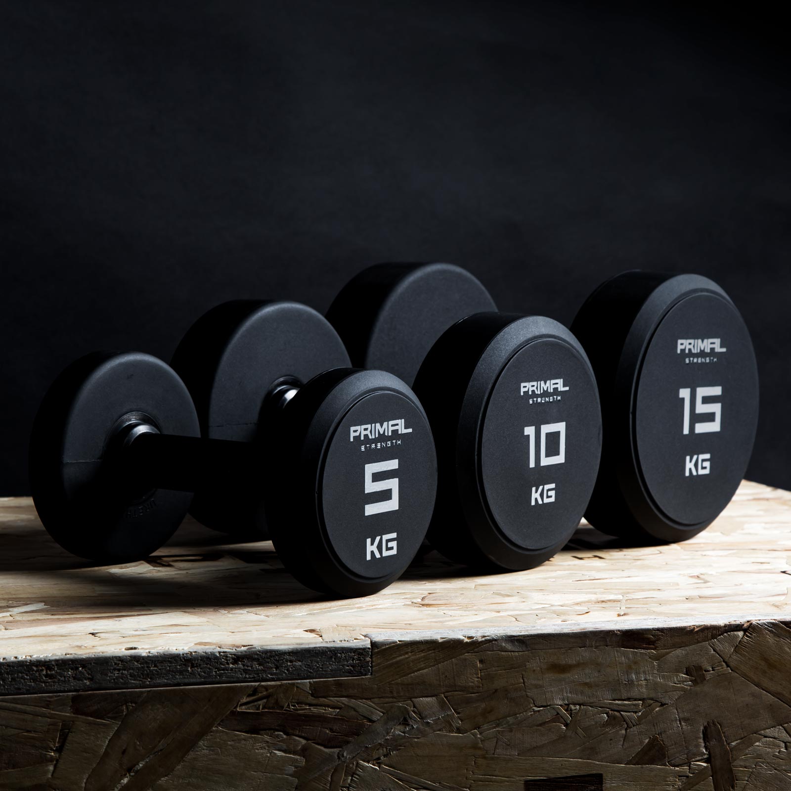three single primal strength black urethane dumbbells on a wooden box