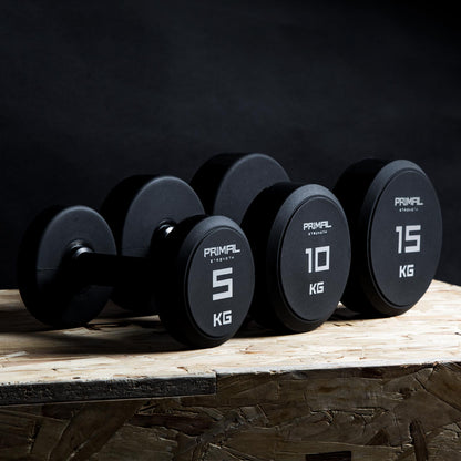 three single primal strength black urethane dumbbells on a wooden box