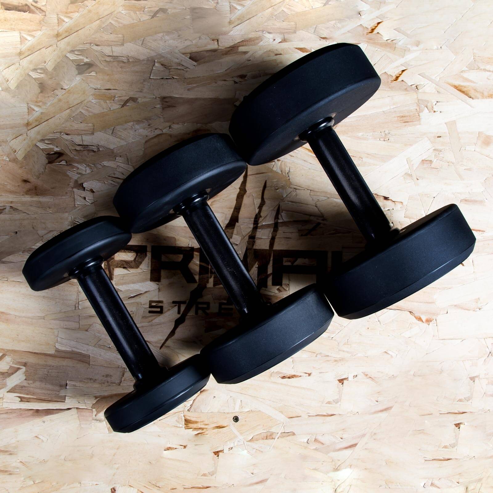 three single primal strength black urethane dumbbells on a wooden box