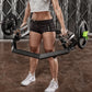 a woman stood straight holding a olympic shrug bar loaded with weight plates